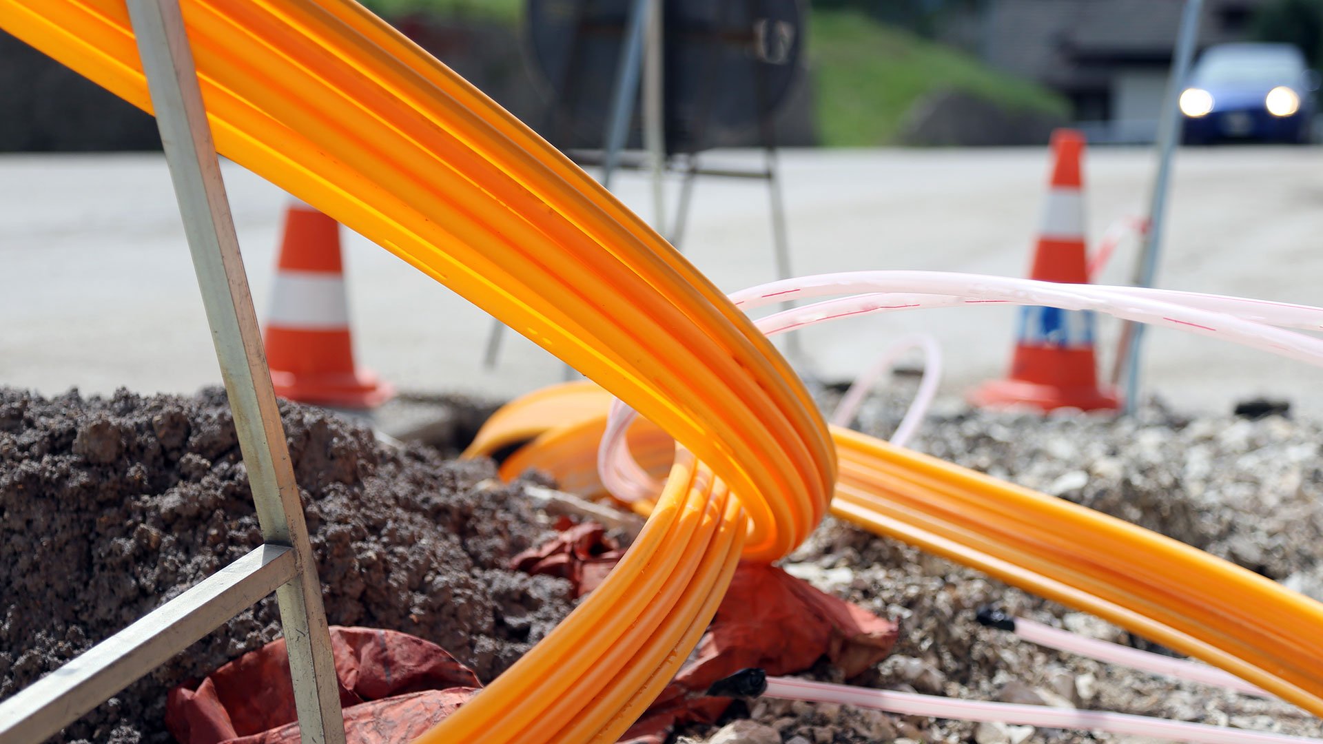 Orange Glasfaser-Leerrohre auf einer Straßenbaustelle mit Absperrkegeln.