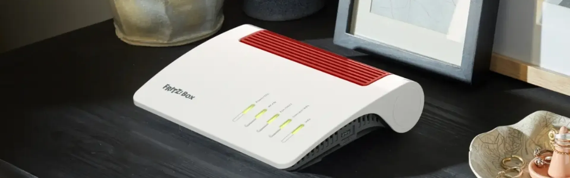 Router mit leuchtenden Statusanzeigen auf einem Regal neben Dekoobjekten.